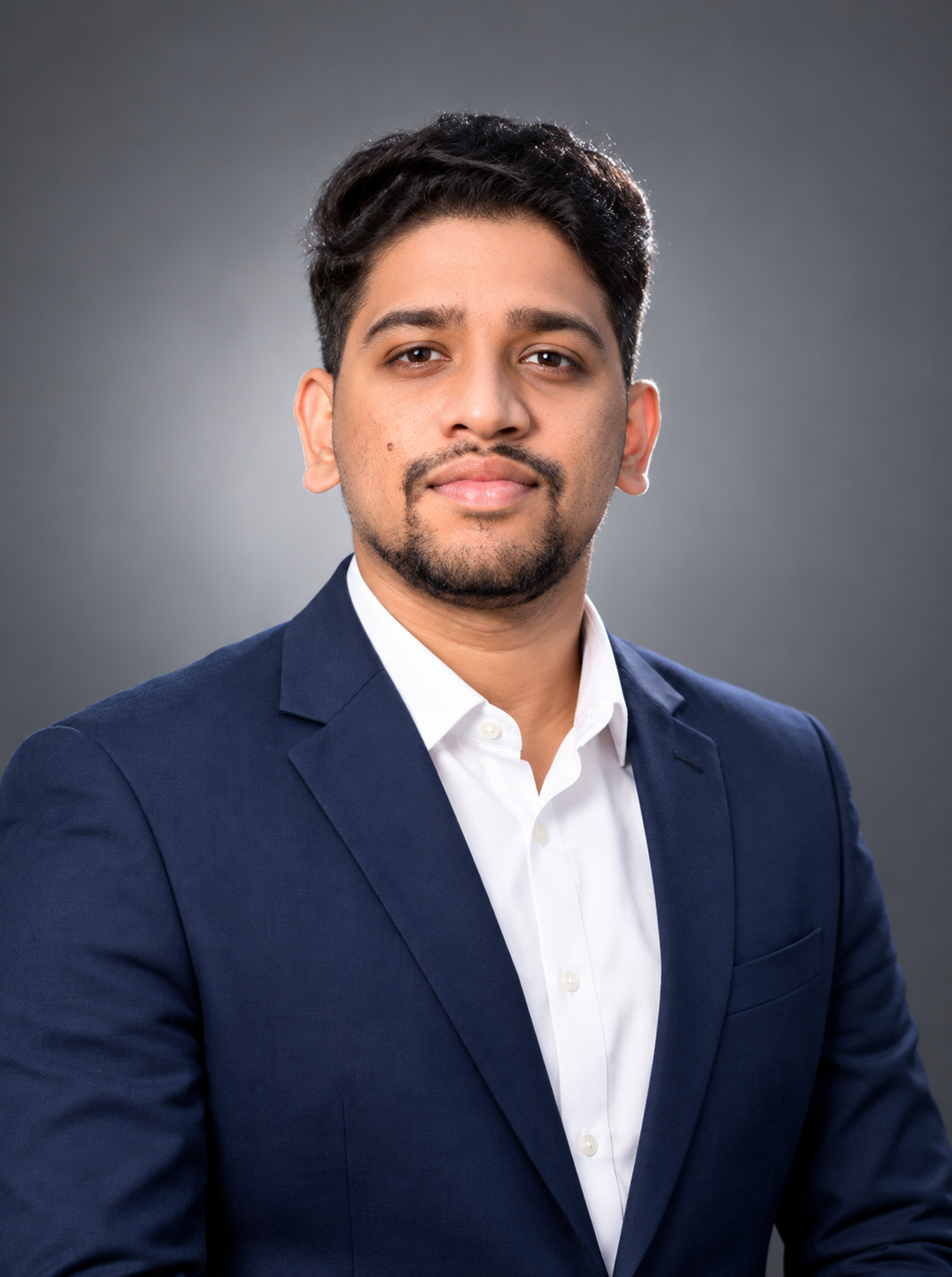 Professional head-and-shoulders headshot in a navy blazer against a soft grey studio backdrop
